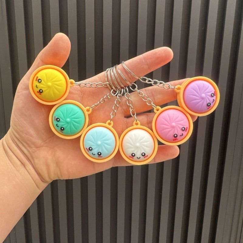 Hand holding six silicone bao bun keychains in steamer basket frames with smiling faces