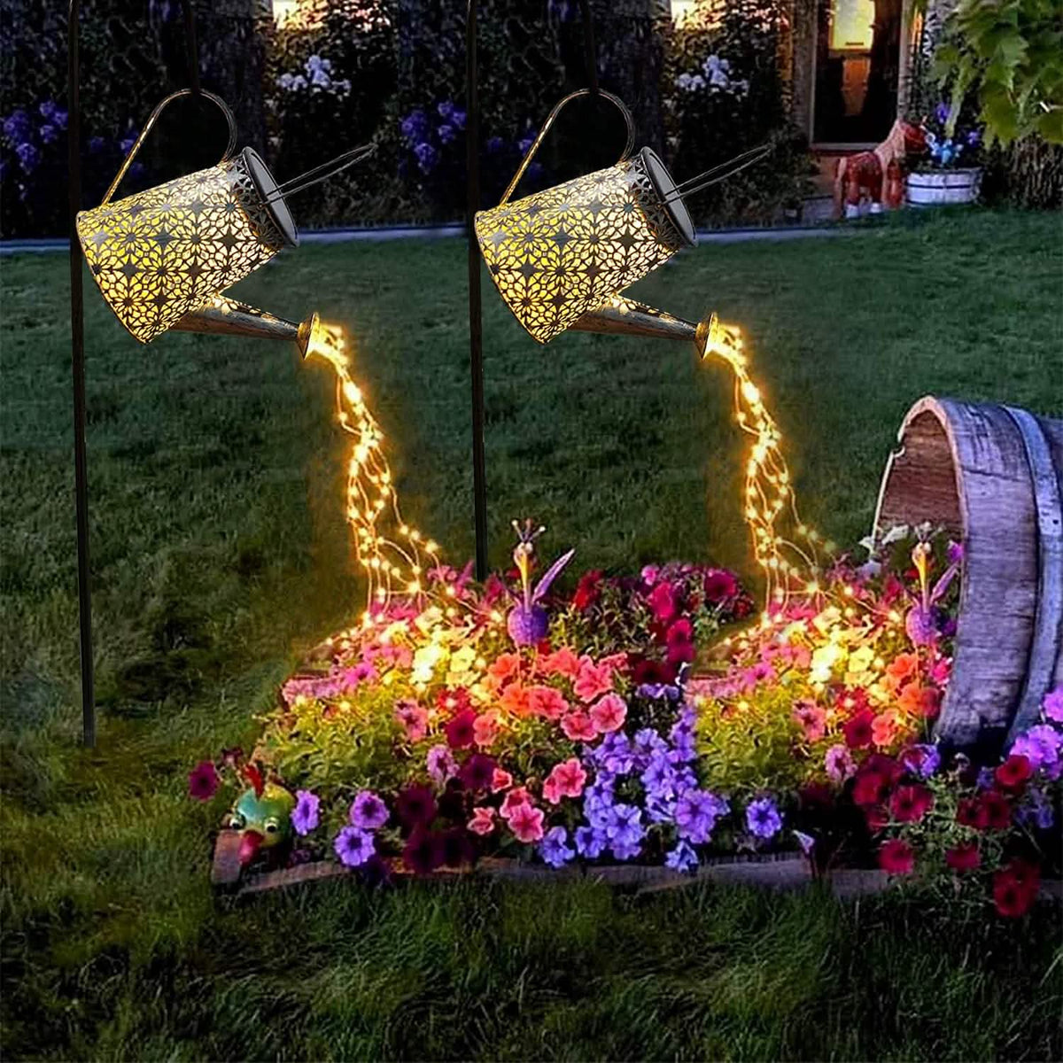 A pair of warm white watering can lights pouring over a garden bed at dusk
