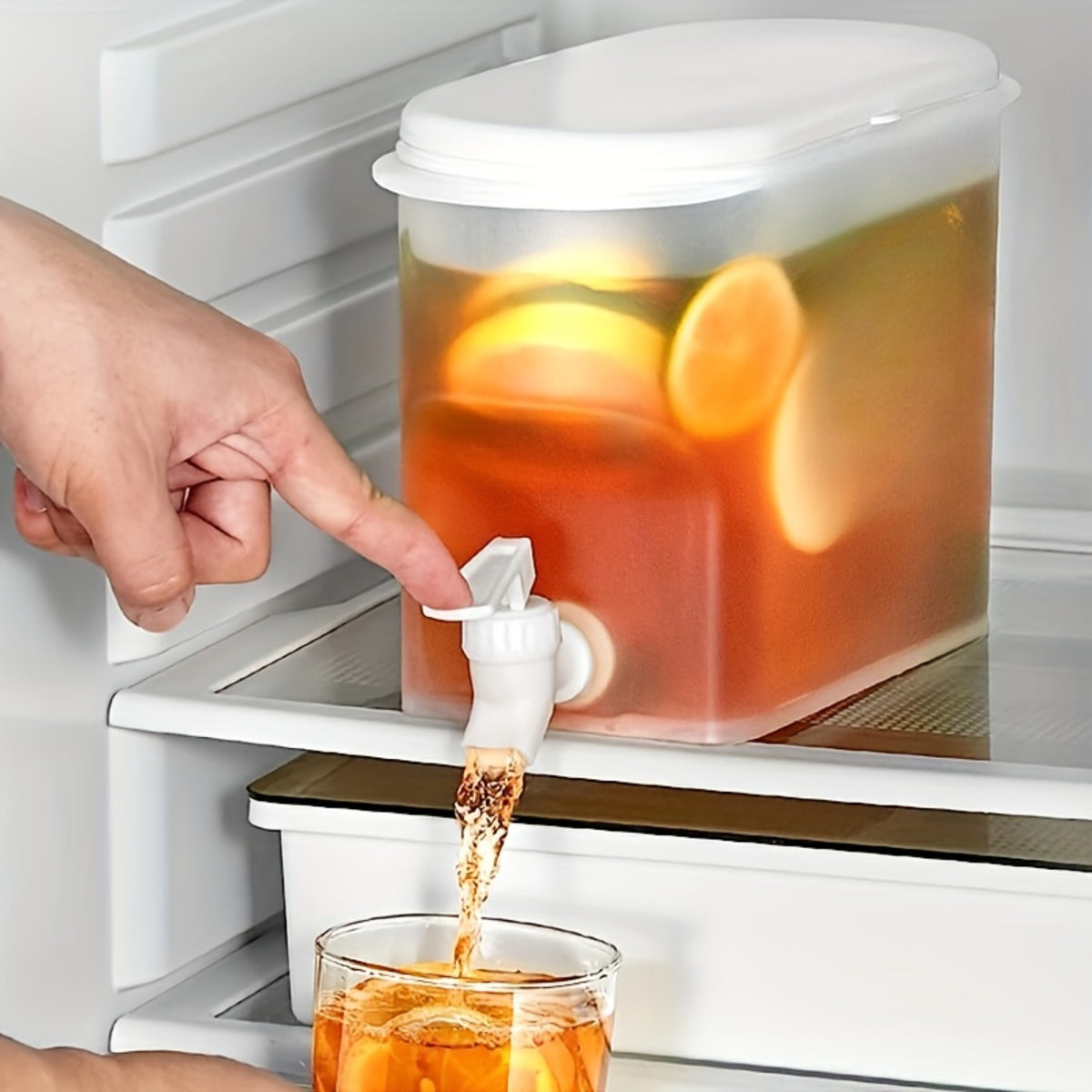 Clear drink dispenser with push tap on a fridge shelf pouring iced tea