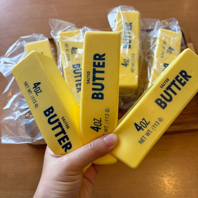 Hand holding several realistic salted butter stick squishy fidget toys