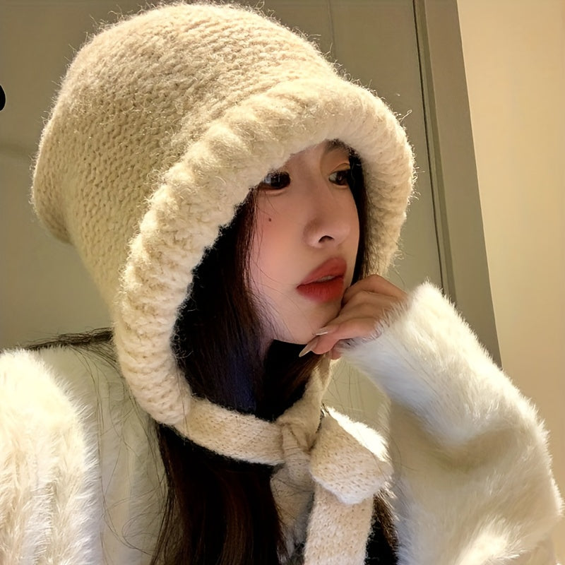 Beige knit earflap hat worn, tied under the chin