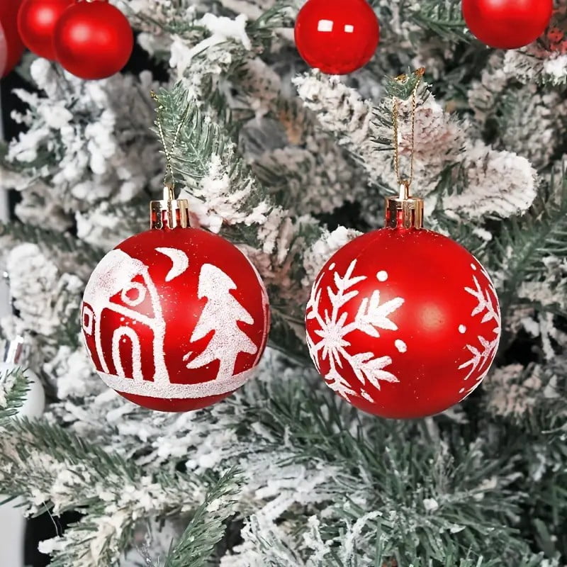 Red balls with a white house and tree and a white snowflake hanging on a flocked tree