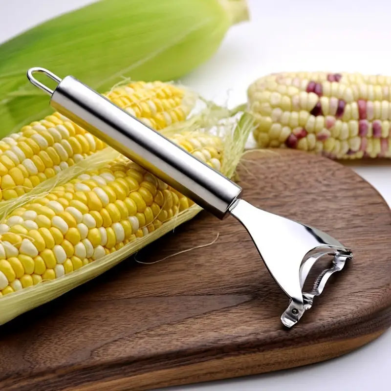 Stainless Steel,Corn Peeler, Planer, Thresher shown on top of a cutting board resting against a corncob