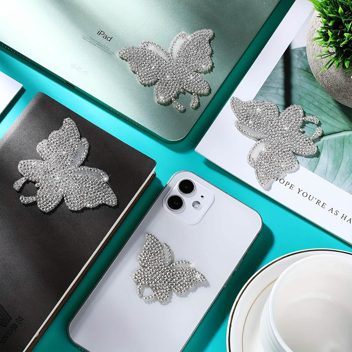 Silver rhinestone butterfly decals shown on a desk, laptop and phone