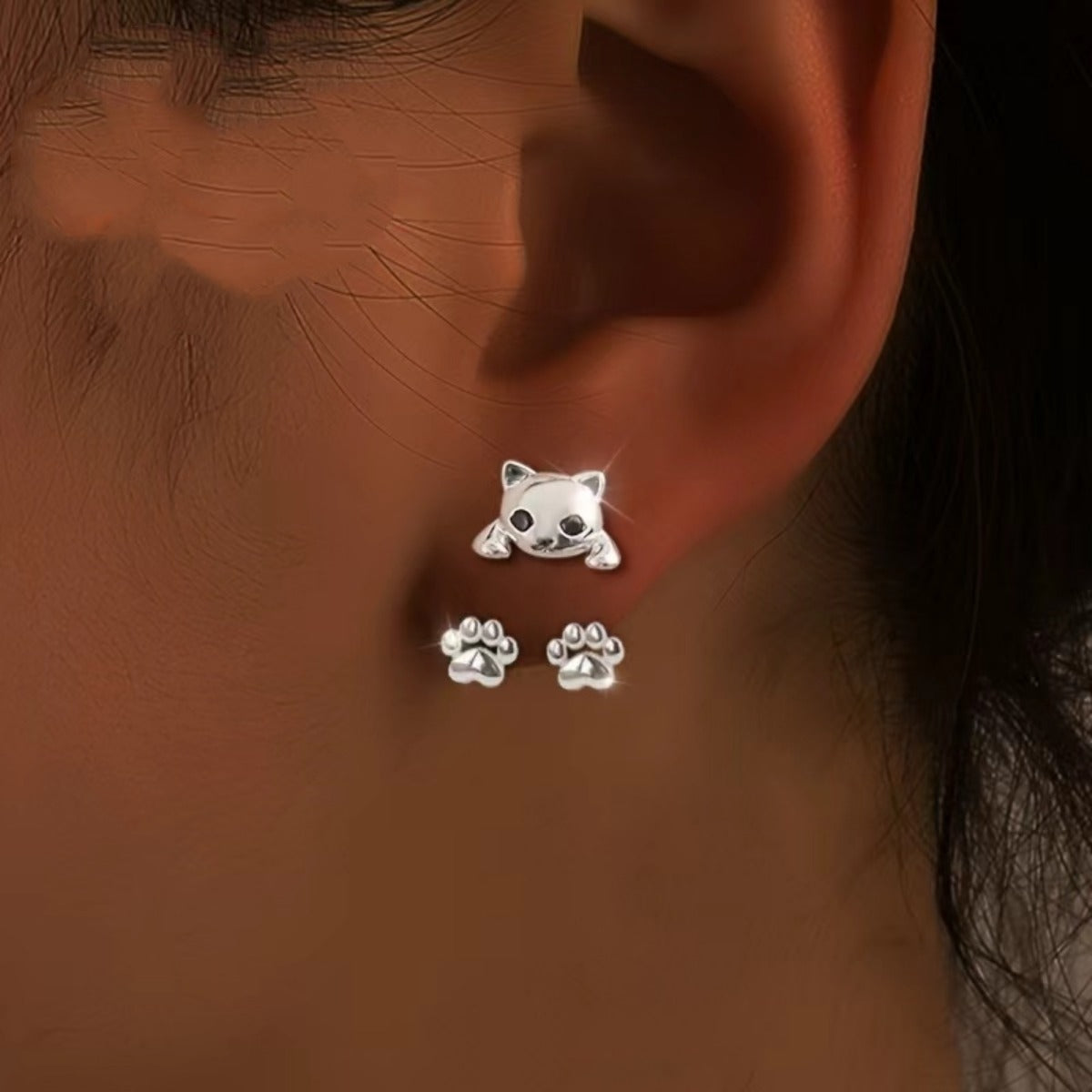 Close view worn on the ear: kitten face on the front of the lobe, two paws sitting just below