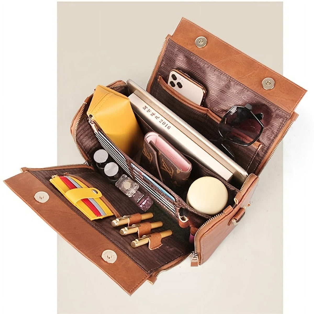 The bag laid open flat with a phone, notebook, purse, sunglasses and cosmetics in the compartments