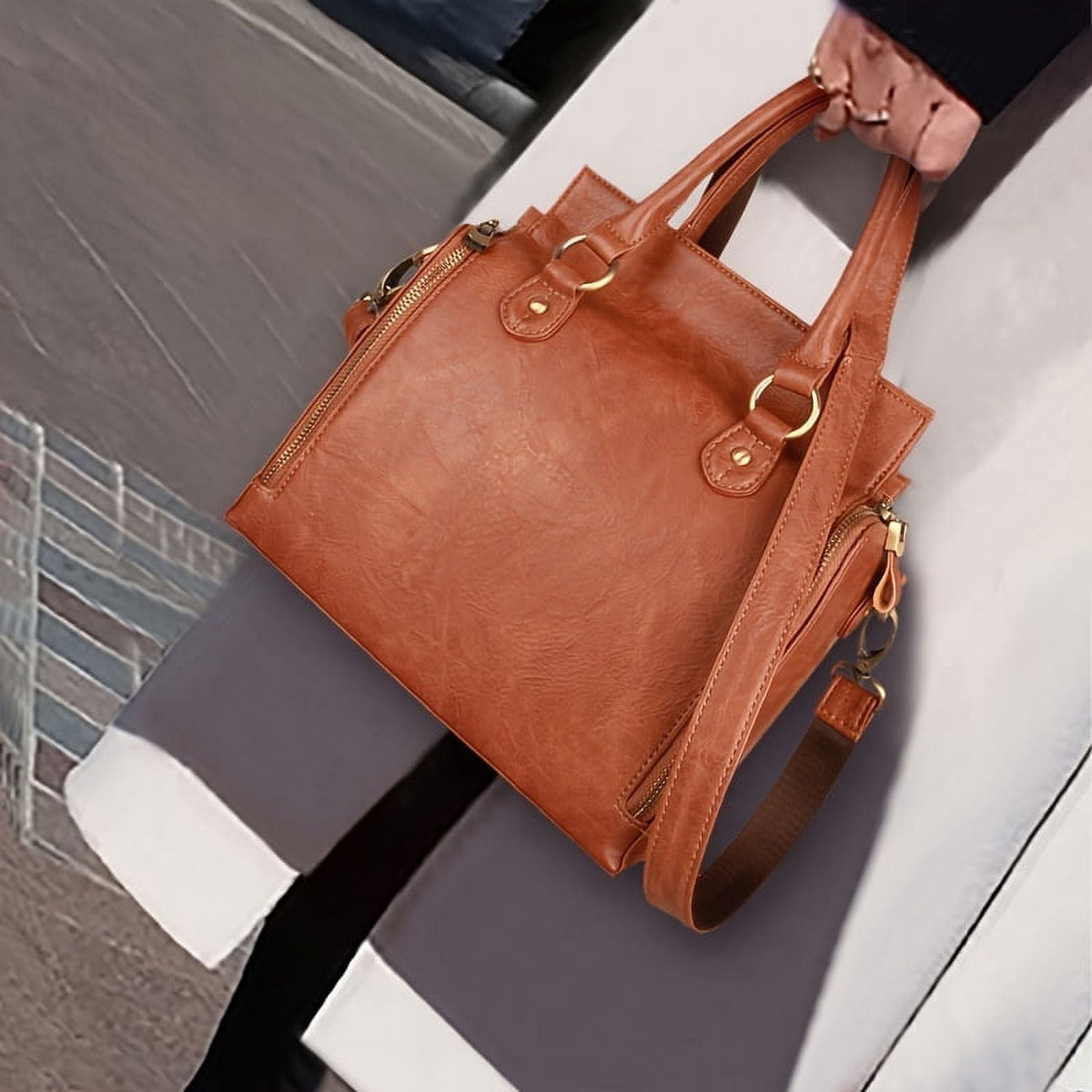 The bag carried by the handle outdoors, showing the grain of the leather and the side zips