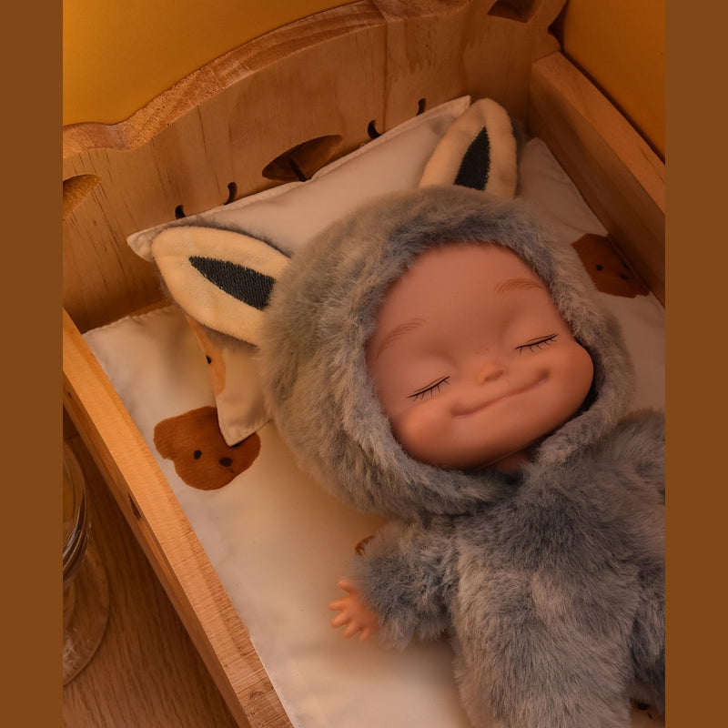 Gray plush onesie doll with eyes closed, resting in a wooden toy bed
