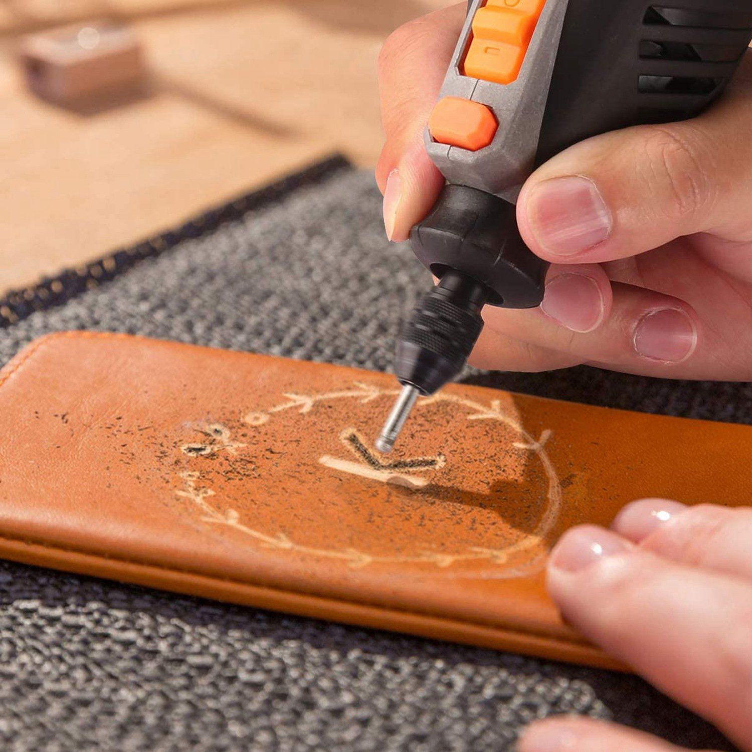 Closeup of a woman's hand holding a Rotary Dremel tool from the 228-Piece Rotary Dremel Accessory Tool Kit engraving the letter "K" on a piece of wood