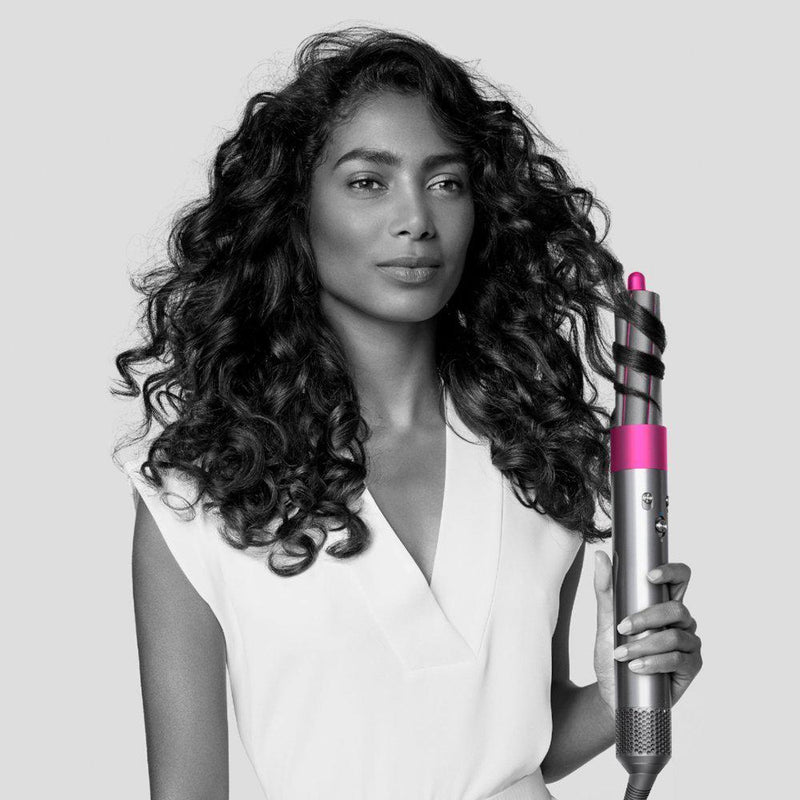 Woman holding a Dyson Airwrap Complete Style For Multiple Hair Types And Styles with her right hand and wrapping her hair with it as a demonstration