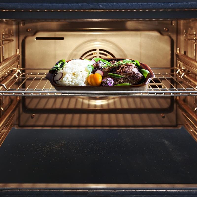 Lit up open oven showing a meat and rice meal in a glass dish with the Heavy-Duty Nonstick Oven Liner for Oven placed underneath to catch drips and splatter