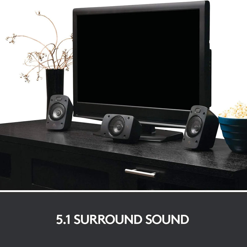Display of three Logitech Z906 5.1 Surround Sound Speaker System speakers in front of a flat-screen tv on black table next to a bowl of popcorn